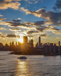 Sea by buildings in city against sky during sunset