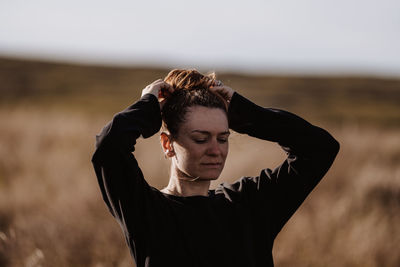 Young woman looking away while standing on field