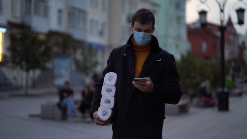 Man wearing mask using mobile phone outdoors