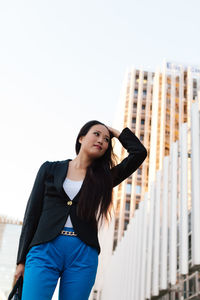 Portrait of young woman looking away against city