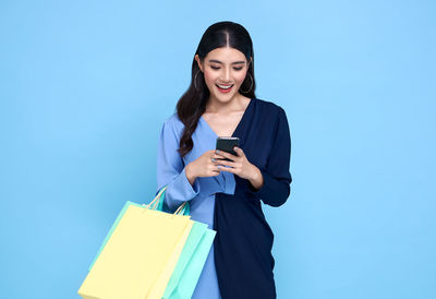 Young woman using phone while standing against blue background
