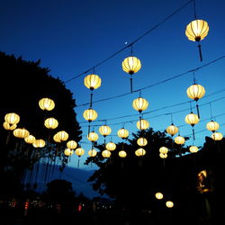 Low angle view of illuminated lanterns hanging against sky at dusk