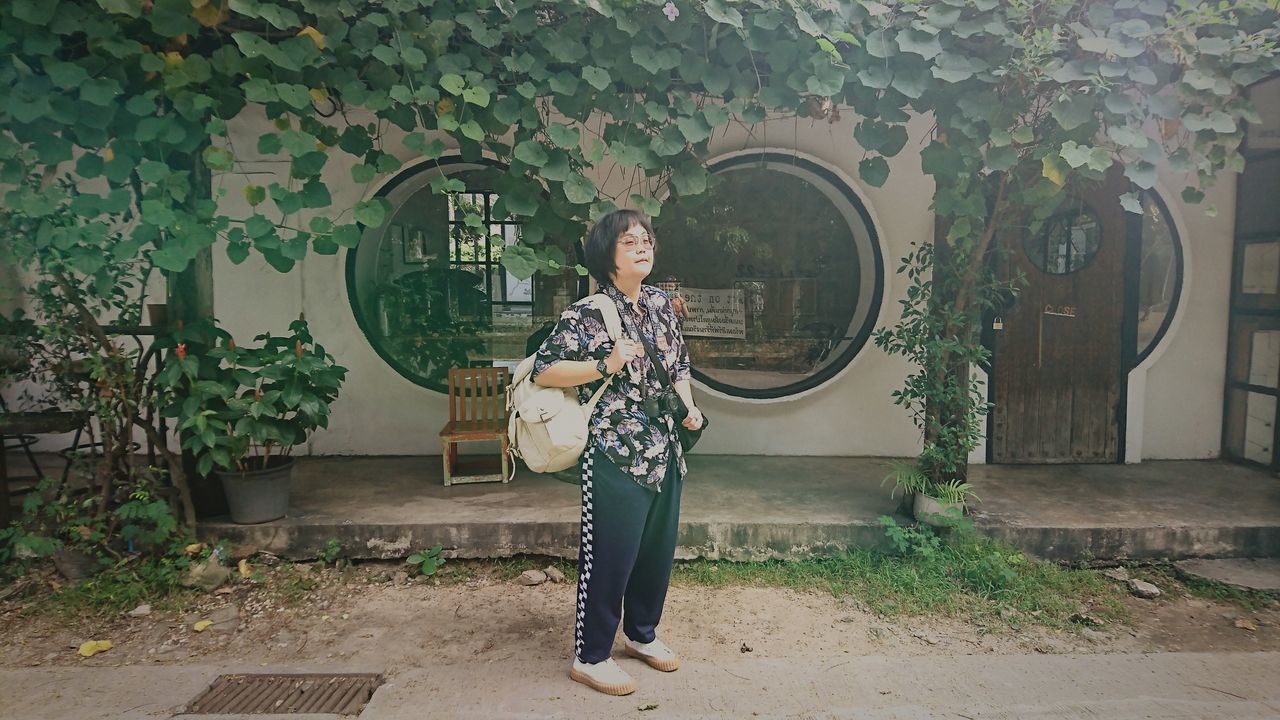 PORTRAIT OF MAN STANDING BY PLANTS