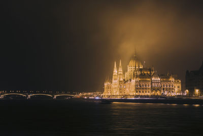 Illuminated bridge over river against sky at night