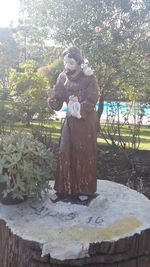 Statue of woman standing by tree against sky