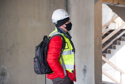 Portrait of thoughtful civil engineer architect wearing hardhat and black face mask at building site