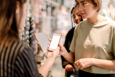 Woman showing phone to saleswoman at fashion store