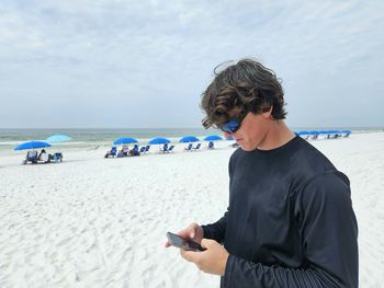 Young man millennial texting on cellphone at beach.