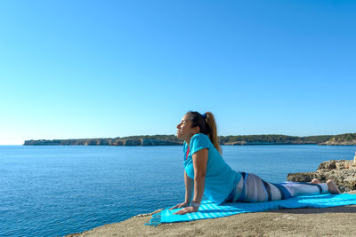 Middle-aged fitness woman outdoors in front of the sea does yoga stretching exercises