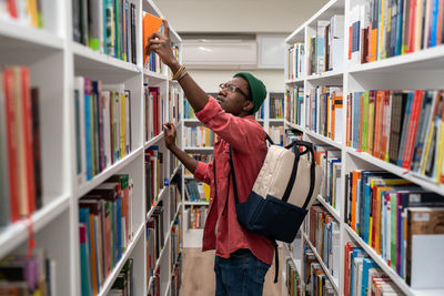 Nerd student african american man choosing book in university library taking it from shelf.