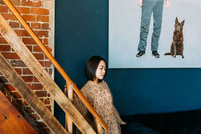 Mid adult woman looking away while standing by railing against wall