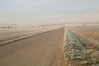 Empty road on landscape against sky during winter