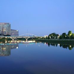 Arch bridge over lake against buildings in city against clear blue sky