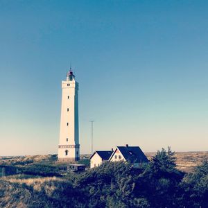 Lighthouse by building against clear blue sky