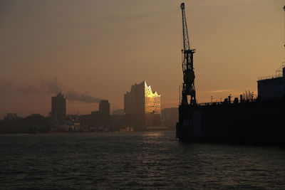 Sea by buildings against sky during sunset