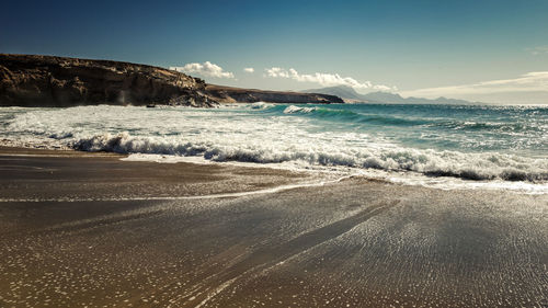 Waves rushing towards shore against sky