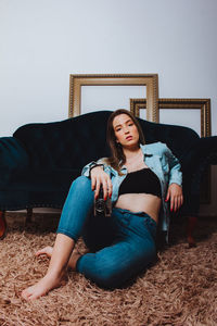 Portrait of woman holding camera sitting by sofa at home