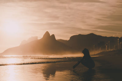 Silhouette woman on sea against sky during sunset