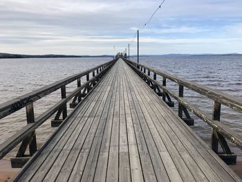 Empty footbridge over sea against sky