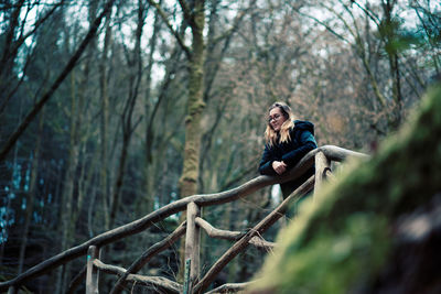 Low angle view of woman leaning on railing at forest