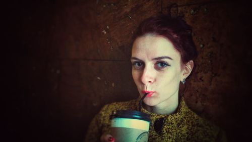 Portrait of young woman drinking coffee against wall