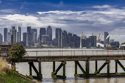 Bridge over river by buildings against sky in city