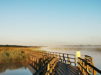 Pier over lake against clear blue sky