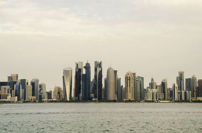 Sea by modern buildings against sky in city