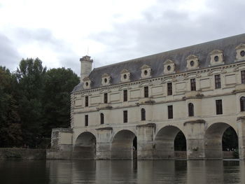 Building by river against cloudy sky