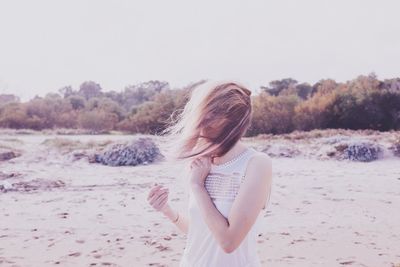 Young woman standing on beach with hair covered face