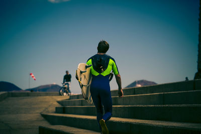 Rear view of man in wetsuit carrying surfboard