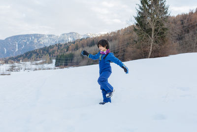 Side view on happy child going down on snow slope in blue winter clothes