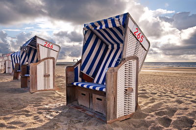 Hooded chairs at beach against sky