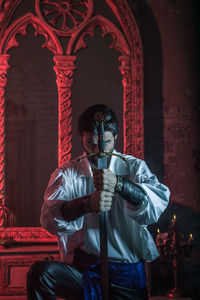 Portrait of man in costume holding sword at abandoned building during night