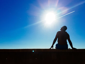Low angle view of man standing against clear blue sky