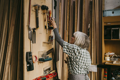 Side view of female senior carpenter removing tool from board at workshop