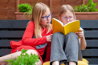 Two school age girls sitting together in garden and doing homework.