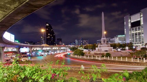 Light trails on street amidst buildings against sky at night