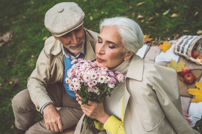 Senior woman holding bouquet while sitting with husband at park