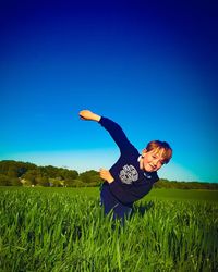 Boy playing on field against clear blue sky