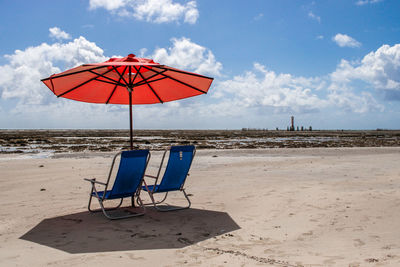 Deck chairs on beach against sky