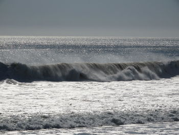 Sea waves splashing on shore against sky