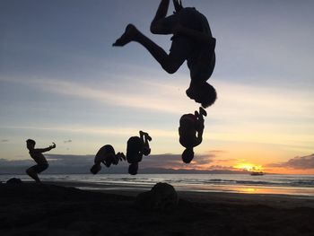 Friends performing somersault at beach against sky during sunset