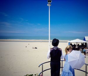 Rear view of children in traditional cloths at observation point near beach against sky