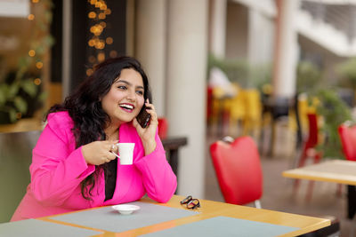 A smiling indian businesswoman is talking on her mobile phone and drinking coffee