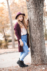 Young woman standing by tree trunk