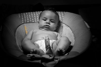 Shirtless baby lying on bed against black background