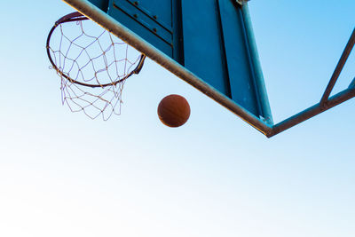 Low angle view of basketball at hoop against clear sky