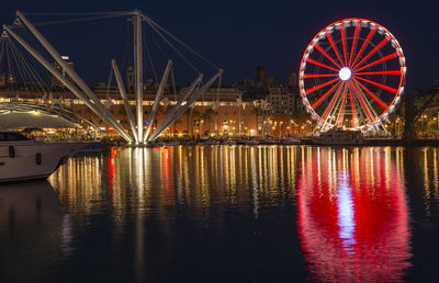 Illuminated ferris wheel by river against sky at night