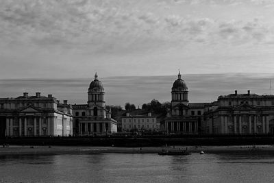 View of buildings by river against sky in city